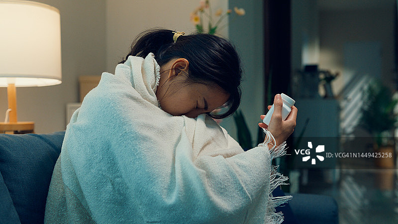 生病的亚洲女孩在沙发上感到寒冷，发烧，拿着药瓶，在家感到无助和孤独，有厌食症症状图片素材
