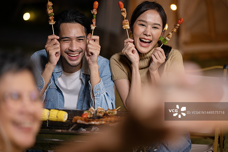 利用科技传播快乐：亚裔老年妇女用智能手机拍摄户外烧烤的家人图片素材