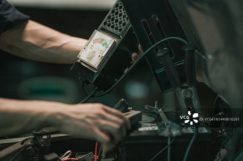 亚洲华裔机械师在汽车修理车间检查电池电量特写图片素材