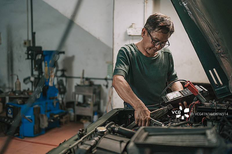 年长的亚洲华裔机修工在汽车修理厂检查电池电量图片素材