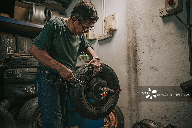 中国资深男 mechanic 在汽车修理店用机器平衡车轮定位轮胎图片素材
