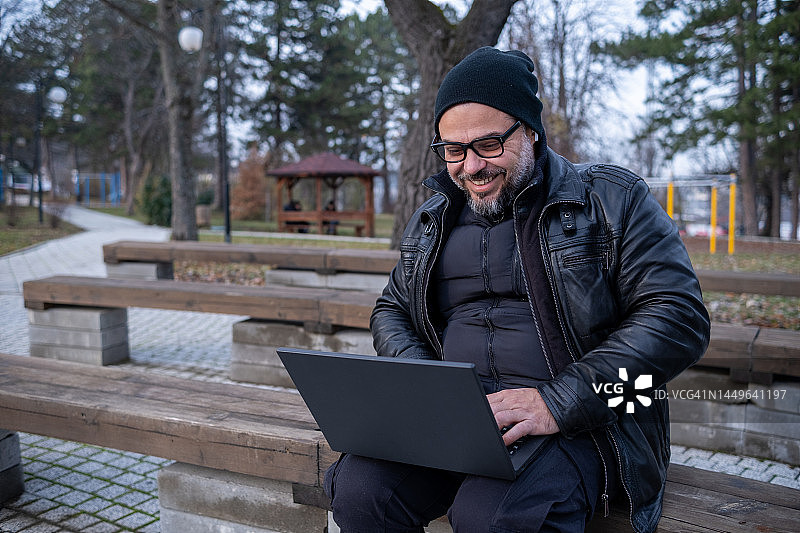 快乐的男人在公园里使用笔记本电脑工作。图片素材