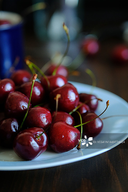 马克杯和盘子里的红色成熟樱桃：在木制餐桌或厨房桌子上，素食、纯素食和生食，以及饮食的概念，从农场到餐桌的道德消费图片素材