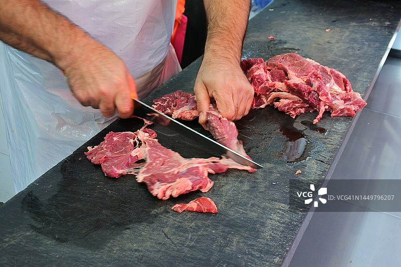 屠夫用长长的锋利刀切割新鲜红肉图片素材