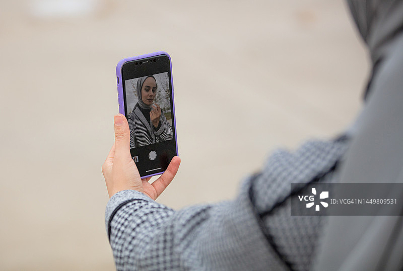 使用手机屏幕化妆的年轻戴头巾女人图片素材