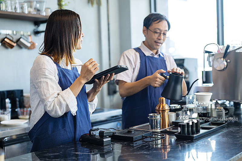 在咖啡店营造吸引顾客的环境：咖啡店主在柜台内讨论图片素材