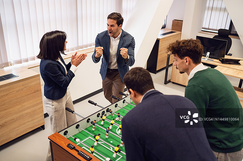 在办公室玩桌上足球并一起玩乐的商务人士图片素材