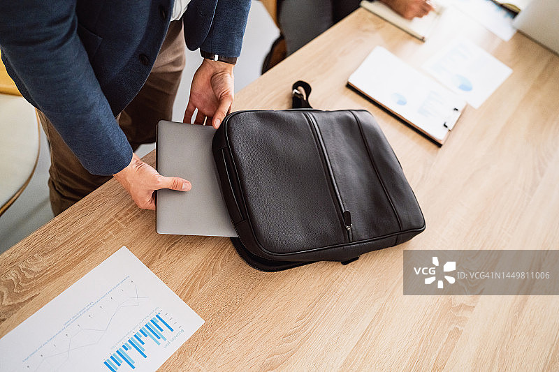 工作场所：一位身份不明的商人将笔记本电脑放入背包图片素材