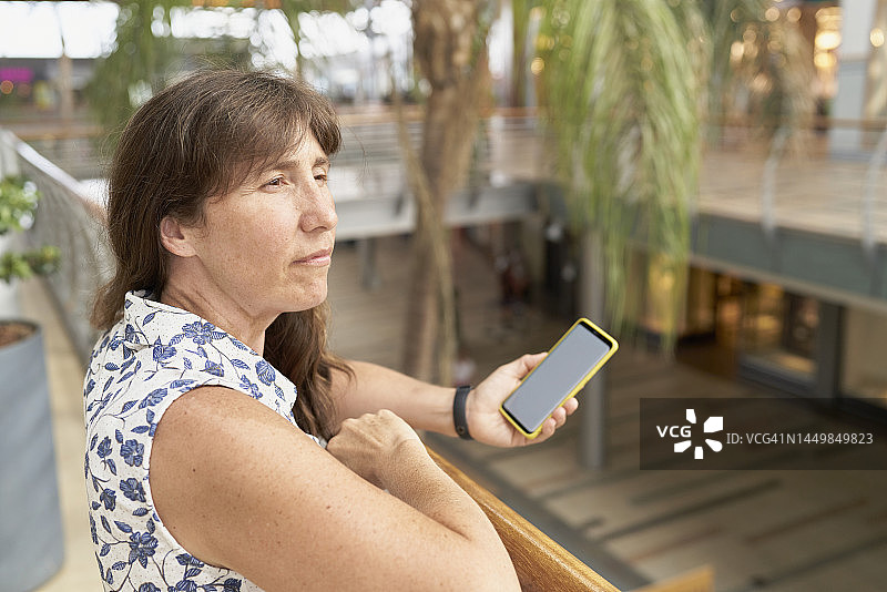 在二楼公寓栏杆上用手机放松的浅棕色头发成年女人图片素材
