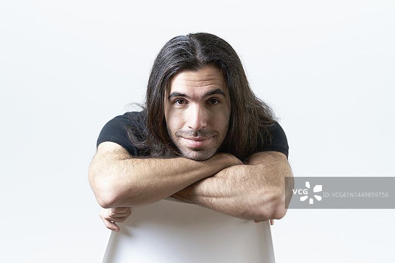 坐在倒置椅子上微笑看着镜头的长发男人图片素材