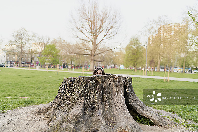 女孩躲在公园树干里玩耍或害怕，看向镜头图片素材
