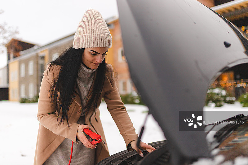 年轻女人试图弄清楚如何在冬天启动汽车图片素材