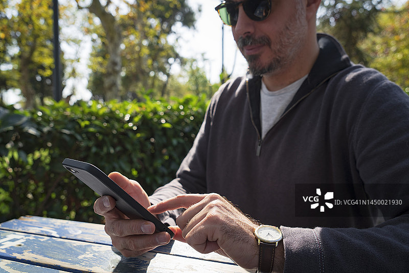 男人坐在人行道咖啡馆的户外使用智能手机图片素材