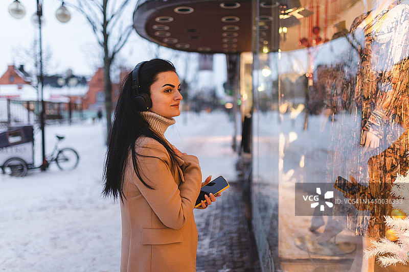 年轻女子在圣诞节期间戴着耳机在橱窗购物图片素材