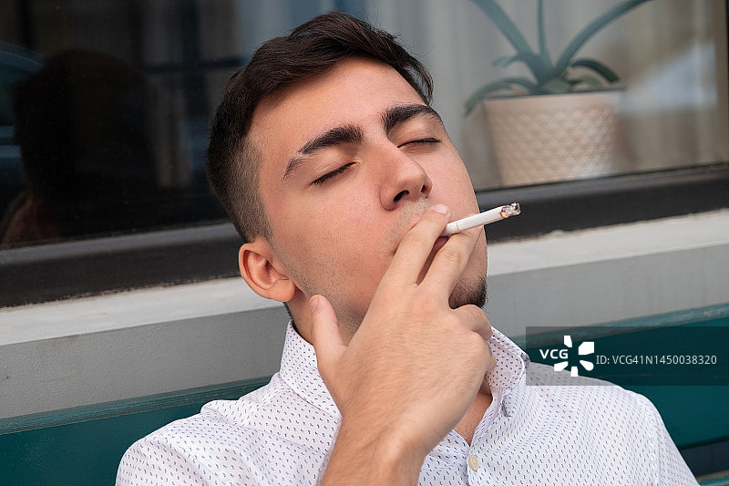 年轻的商人肖像。白衬衫的白人男子。现代商务人士，成功的企业家在休息时离开办公室，手里拿着香烟抽烟。尼古丁成瘾，不健康的生活方式的概念。图片素材