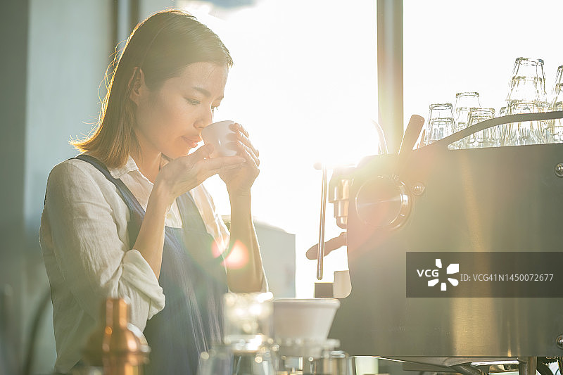 用咖啡的品味和品质维持强大的客户群。一位日本咖啡店女店主手捧一杯咖啡，闻着新鲜烘焙的咖啡，以控制每一杯咖啡的质量。图片素材