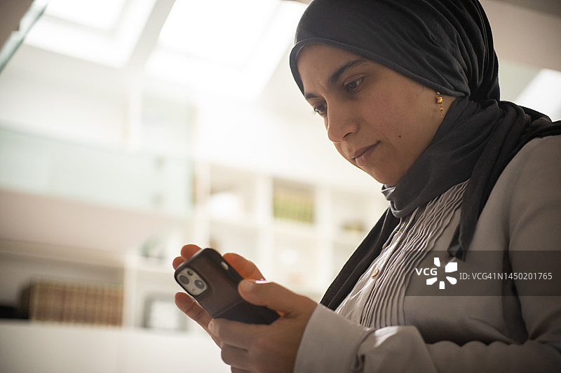 在室内使用智能手机的穆斯林女人图片素材