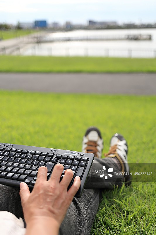 男人在户外草地上用电脑键盘打字图片素材