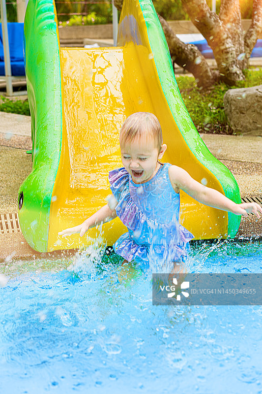 快乐可爱女婴在水上滑梯上滑入泳池图片素材