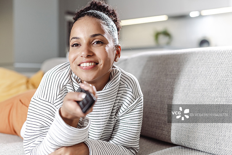 年轻女人拿着遥控器选择电视节目图片素材