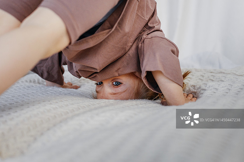 可爱的小女孩在床上做瑜伽，练习下犬式，学习向前翻滚图片素材