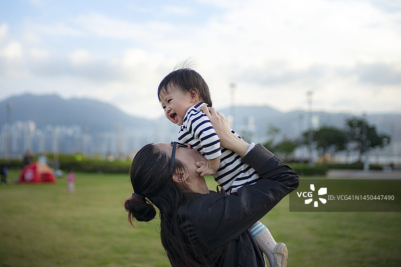 快乐的亚洲母亲和女儿在公园里享受快乐的家庭时光，母亲将女婴抱在空中图片素材