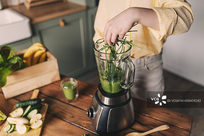 健康饮食：在家制作绿色蔬菜奶昔的年轻女人图片素材