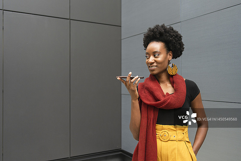 微笑的女人在灰色墙前用免提电话图片素材