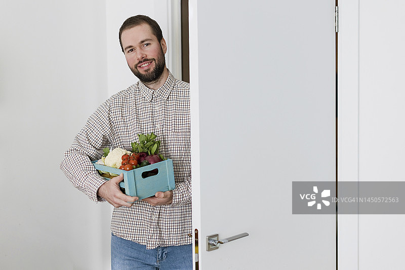 站在门口拿着一箱新鲜蔬菜的微笑男人图片素材