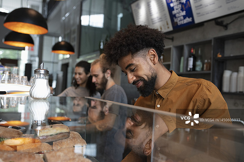 微笑的咖啡师站在咖啡馆的展示柜后图片素材