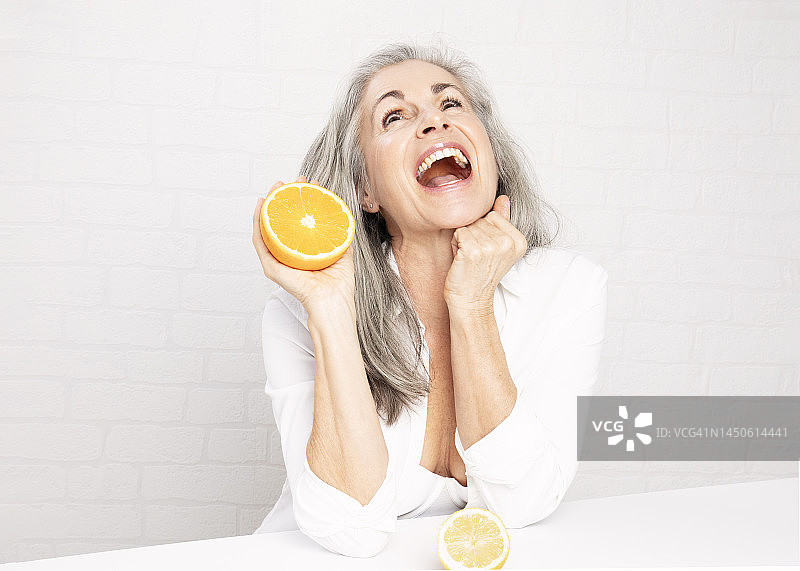 快乐的中年妇女坐在墙前，面前放着橘子图片素材