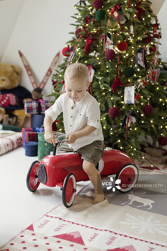 男孩在圣诞树旁玩玩具车图片素材