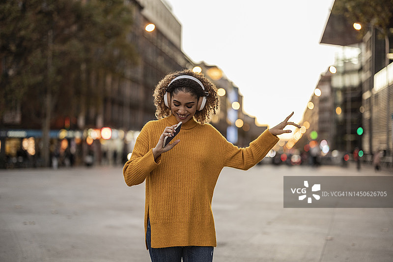 年轻女子在人行道上用无线耳机听音乐跳舞图片素材