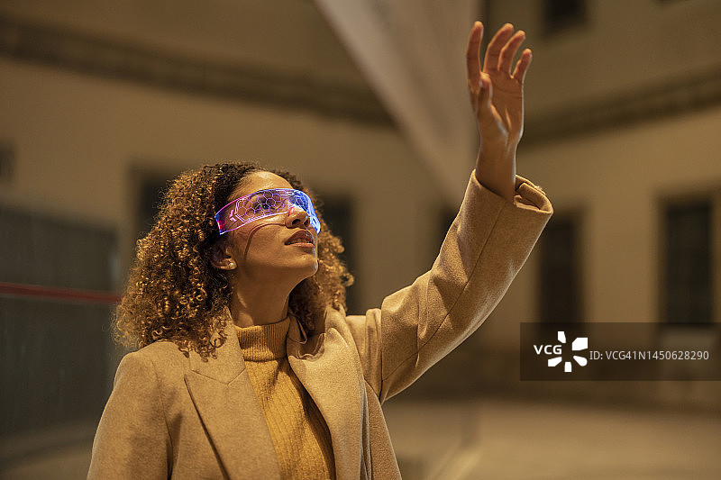 戴着智能眼镜在夜晚做手势的年轻女人图片素材