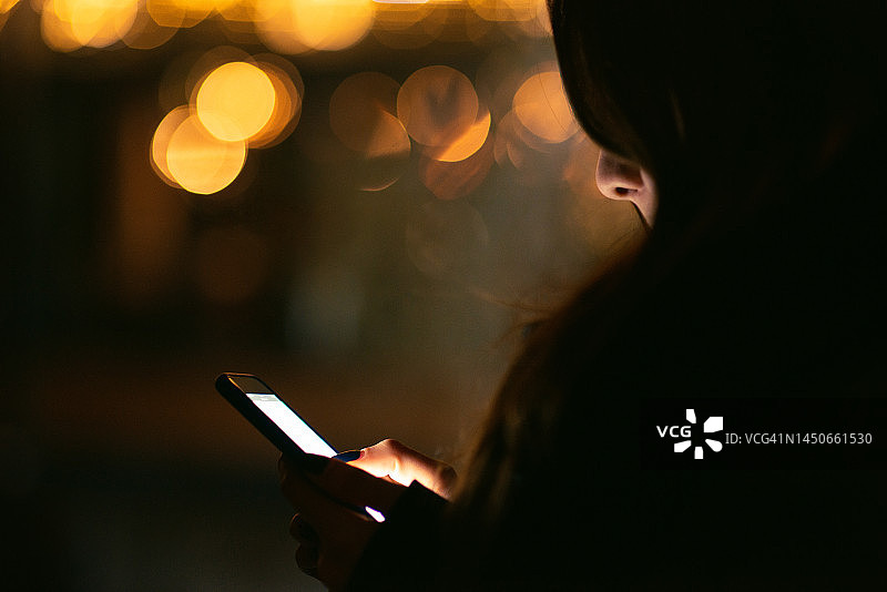 夜晚在市中心使用智能手机的年轻女商人，背景是灯火通明的城市图片素材