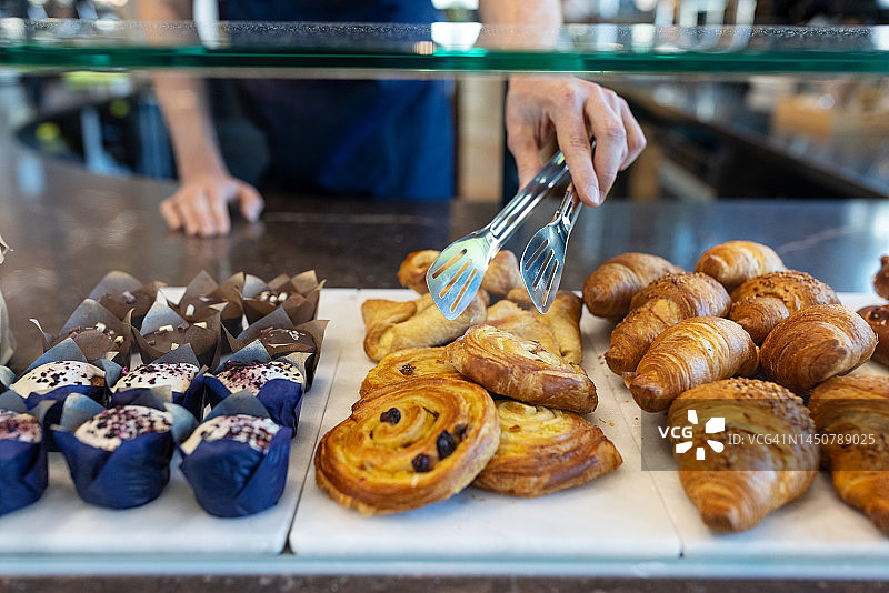咖啡馆工作人员用食物夹从展示柜中取出圆形烘焙糕点图片素材