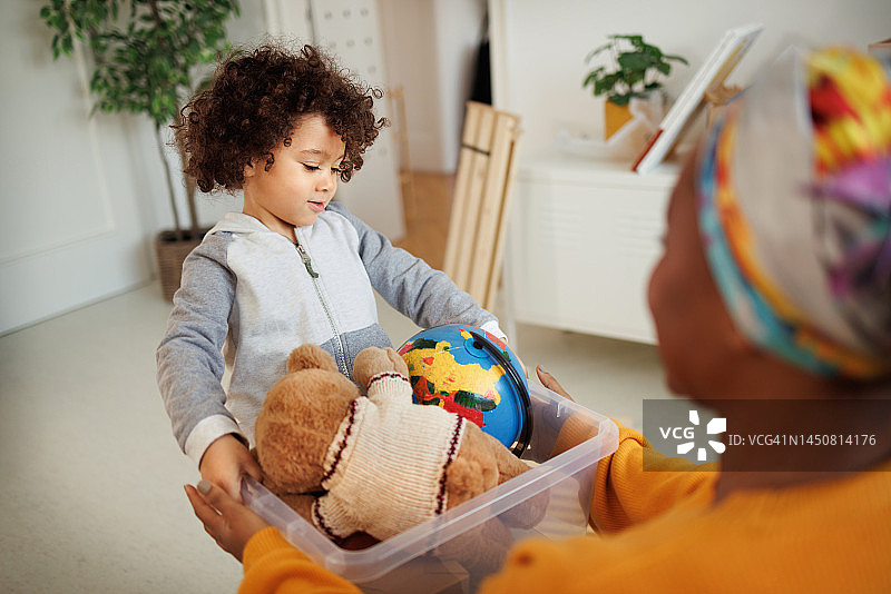 可爱的小男孩在舒适的公寓里给妈妈一盒玩具图片素材