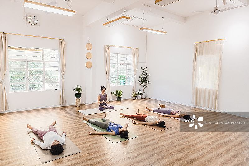 亚洲女性在瑜伽垫上休息，教练手持西藏磬钹图片素材