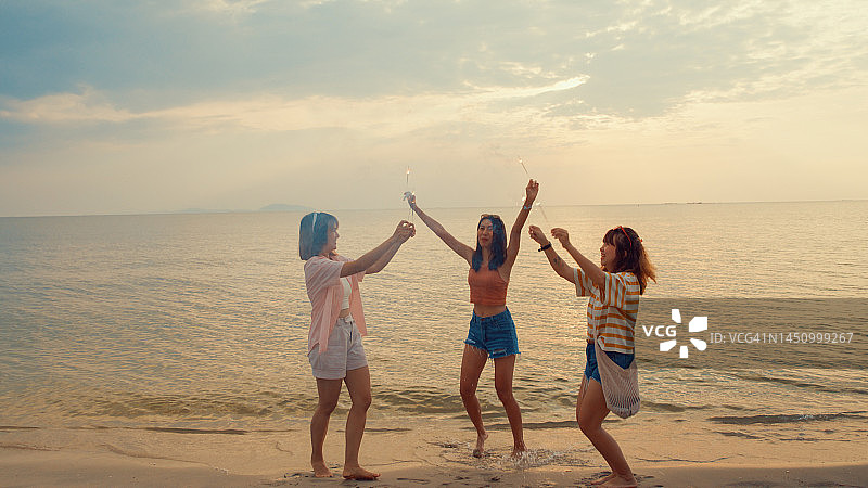 一群亚洲年轻女性在热带海滩上庆祝，手持烟花图片素材