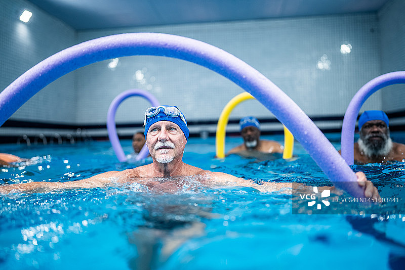 在游泳池用游泳棒锻炼的年长男人图片素材