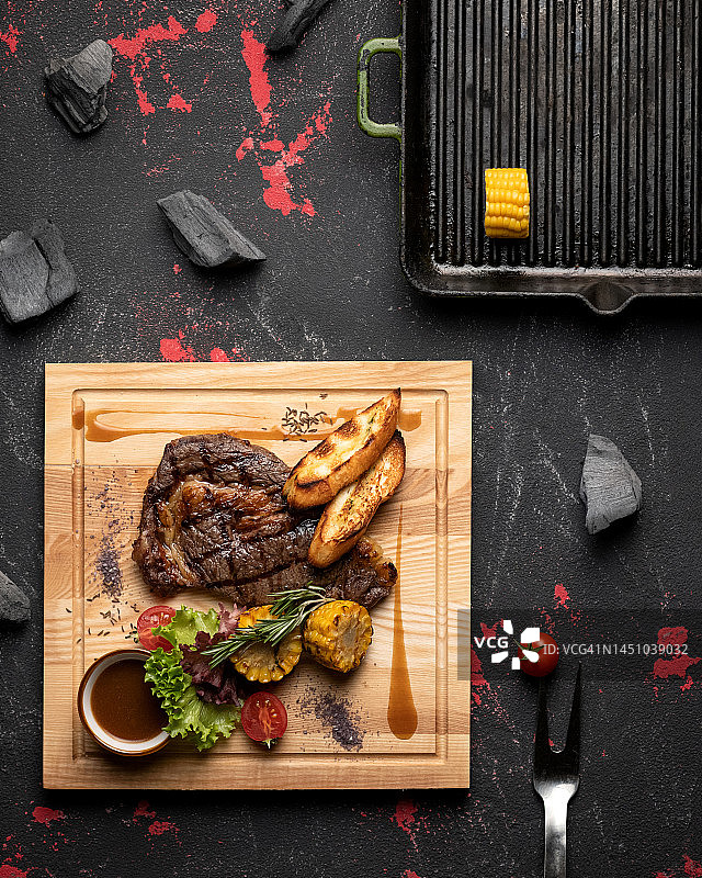 烤牛排配沙拉、酱汁、土豆和烤玉米，木板盛装图片素材