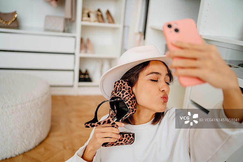 戴帽子的积极女性自拍，并发送飞吻，同时用豹纹鞋作为手机放在耳边图片素材