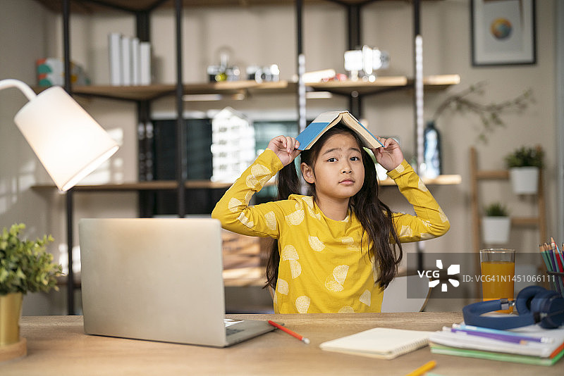 快乐可爱的小女孩用书遮住头对着镜头微笑图片素材