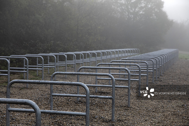 雾蒙蒙的秋日湖岸边，一排空旷的金属自行车架图片素材