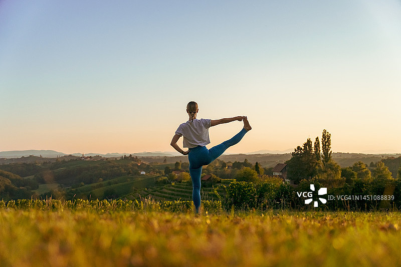 在风景中练习手抓大脚趾姿势的女瑜伽士的背影图片素材