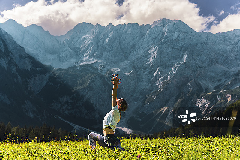 女人在草地上练习新月式，背景是雄伟的山脉图片素材