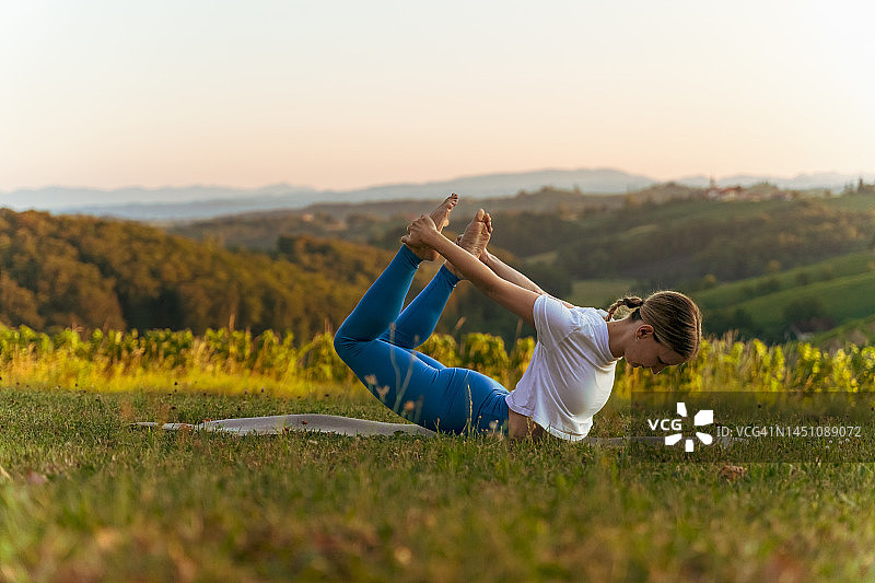 日出时在风景中练习弓式瑜伽的女子图片素材