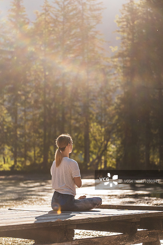 在森林湖边码头上以祈祷姿势冥想的女人图片素材