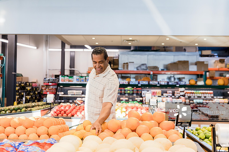 快乐的中年男人在小型市场挑选柑橘类水果图片素材
