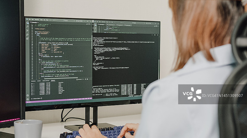 年轻亚洲女性软件开发人员使用电脑编写代码，坐在办公桌前，多个屏幕在家远程工作特写图片素材